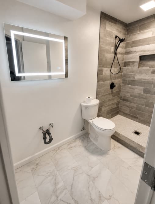 Finished bathroom with a toilet, tiled shower, and illuminated mirror